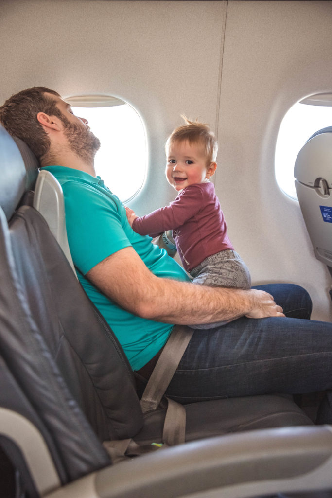 Happy baby sitting on sleeping dad on airplane