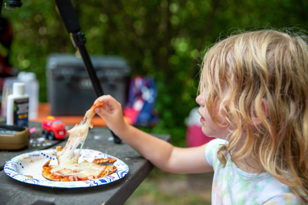 4 year old eating a pepperoni naan pizza cooked over campfire