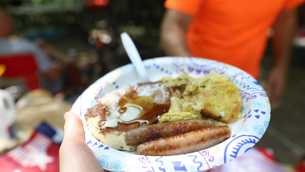 Camping breakfast plate of sausage, pancakes, and eggs cooked over campfire