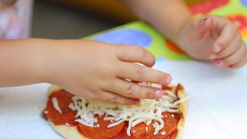4 year old assembling a naan pizza to cook over campfire | camping meals for kids