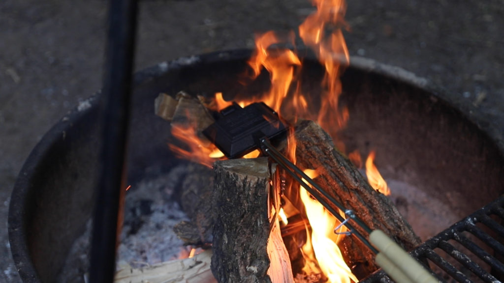 Camp cooker filled with an apple camp pie and being cooker over the campfire