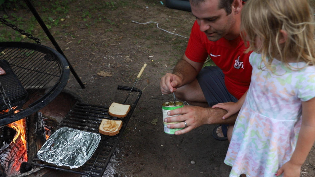 Dad and daughter cooking an apple camp pie together over the campfire
